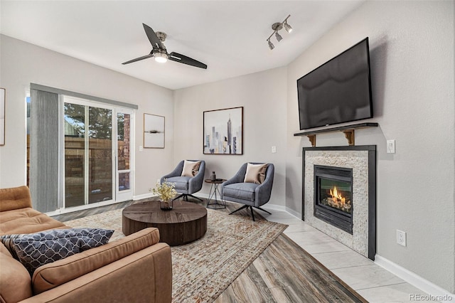 living room with light wood finished floors, ceiling fan, baseboards, and a tile fireplace