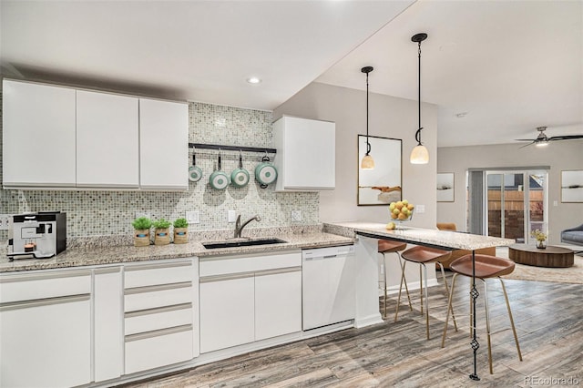 kitchen with decorative light fixtures, backsplash, white cabinets, white dishwasher, and a sink