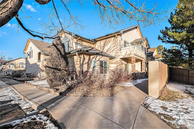 view of property exterior featuring a balcony, stone siding, fence, and stucco siding