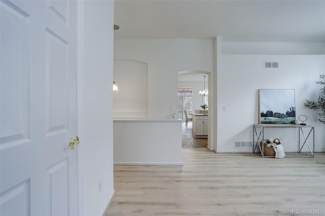 hallway with light wood finished floors, visible vents, and arched walkways