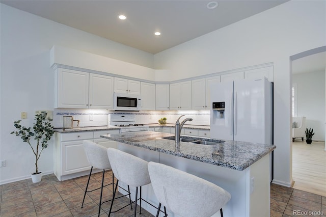 kitchen with light stone counters, white appliances, a sink, white cabinets, and backsplash