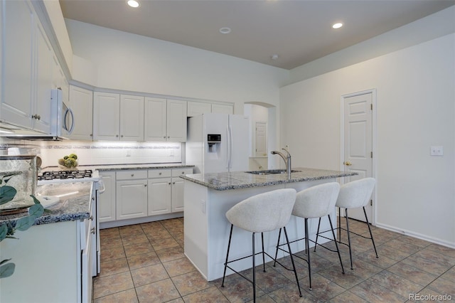 kitchen with white refrigerator with ice dispenser, arched walkways, stainless steel microwave, gas range oven, and a sink