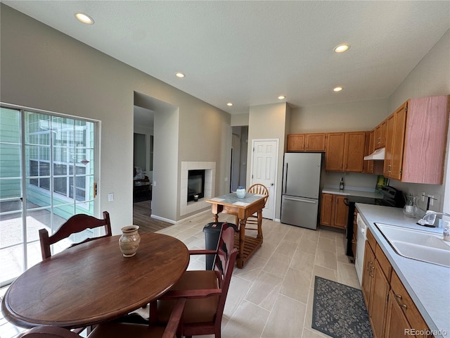 kitchen with a sink, light countertops, electric stove, freestanding refrigerator, and under cabinet range hood
