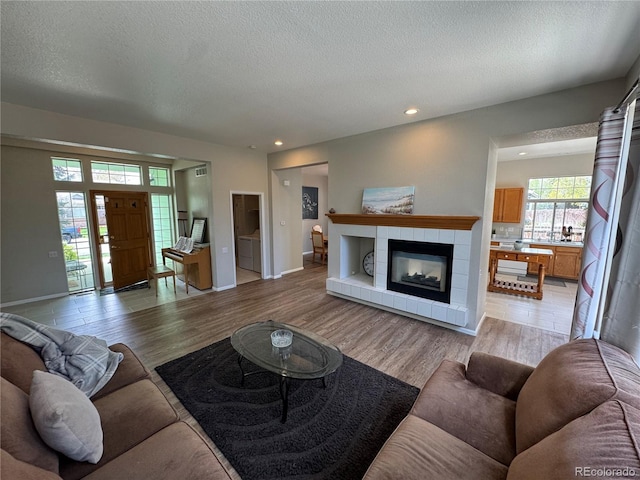living area featuring light wood-style flooring, recessed lighting, a textured ceiling, and a tile fireplace