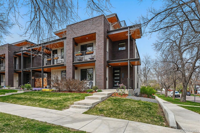 contemporary house featuring a front lawn, brick siding, and a balcony
