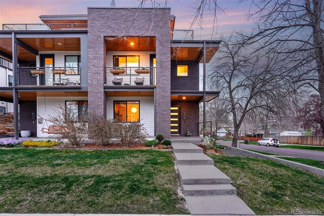 contemporary home featuring brick siding, a balcony, and a front lawn