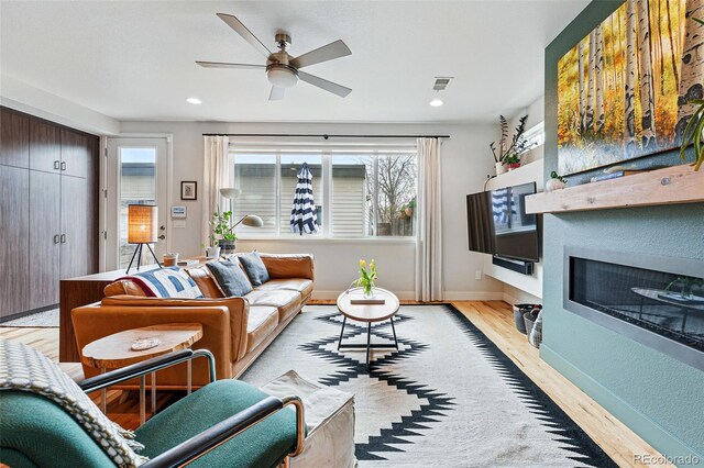 living area with ceiling fan, a fireplace, recessed lighting, light wood-type flooring, and visible vents
