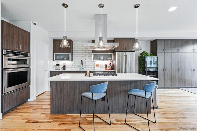 kitchen featuring dark brown cabinets, a breakfast bar area, stainless steel appliances, light wood-type flooring, and tasteful backsplash