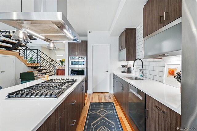 kitchen featuring light wood-type flooring, light countertops, ventilation hood, and appliances with stainless steel finishes
