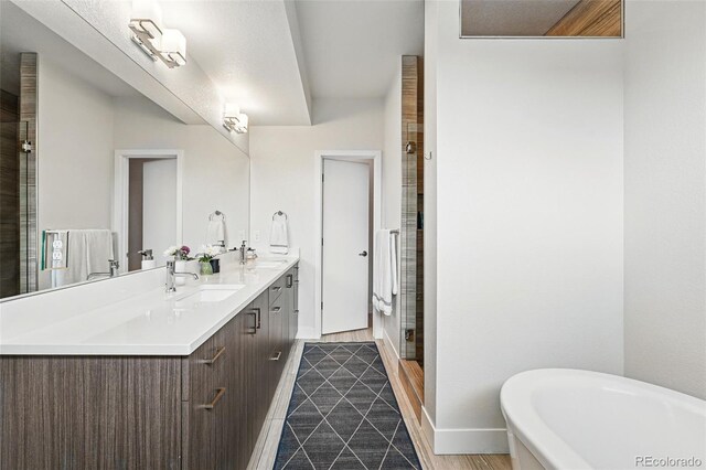 full bathroom with double vanity, baseboards, a freestanding bath, a sink, and a stall shower
