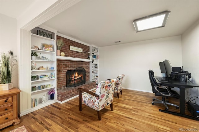 office space featuring built in features, a brick fireplace, and light hardwood / wood-style floors