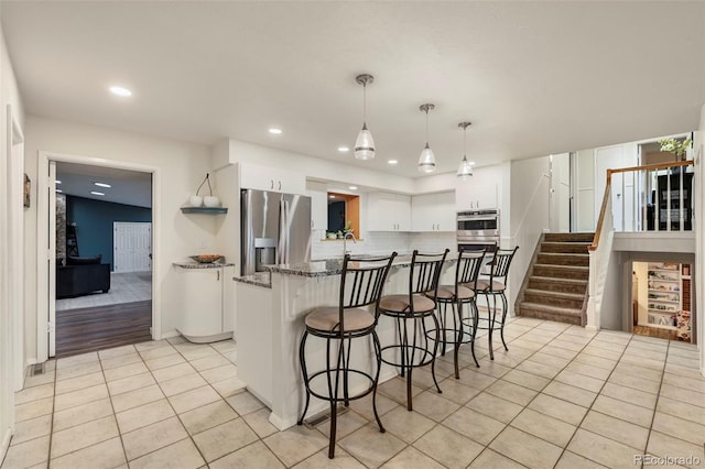 kitchen with dark stone counters, light tile patterned floors, decorative light fixtures, appliances with stainless steel finishes, and white cabinets