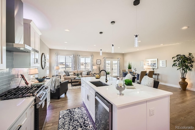 kitchen featuring wall chimney exhaust hood, stainless steel appliances, a kitchen island with sink, sink, and pendant lighting