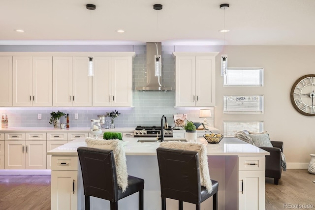 kitchen with white cabinets, wall chimney range hood, hanging light fixtures, and light hardwood / wood-style flooring