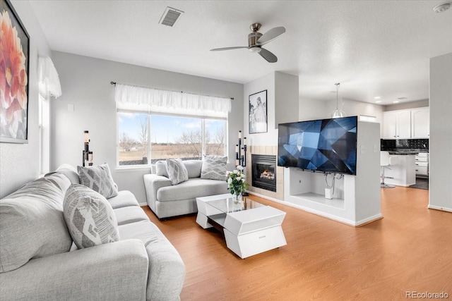 living area with light wood-style floors, a tile fireplace, visible vents, and a ceiling fan