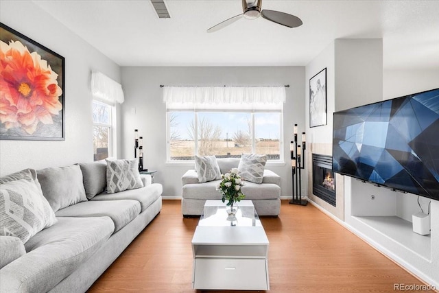 living area featuring light wood-style floors, baseboards, visible vents, and a glass covered fireplace