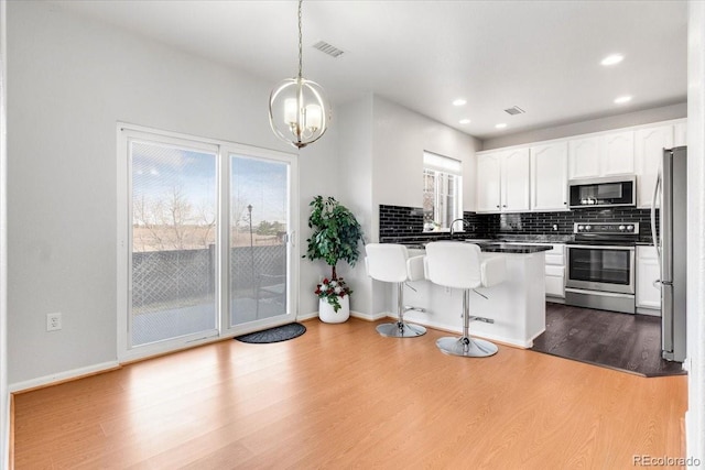 kitchen featuring dark wood finished floors, stainless steel appliances, backsplash, white cabinetry, and a kitchen breakfast bar