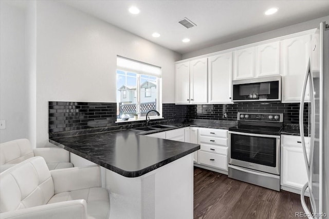 kitchen featuring a peninsula, a sink, appliances with stainless steel finishes, dark wood-style floors, and dark countertops