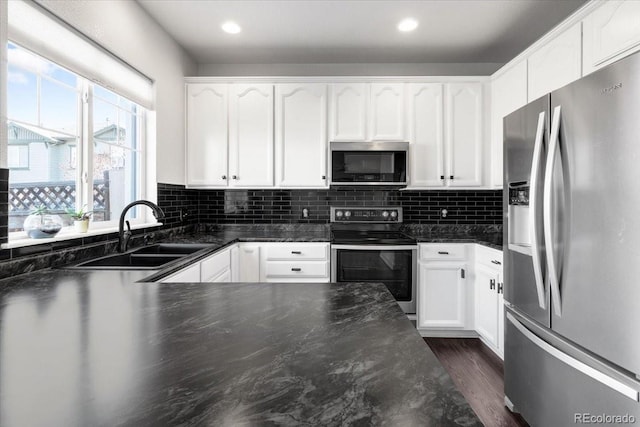 kitchen with appliances with stainless steel finishes, white cabinets, a sink, and backsplash