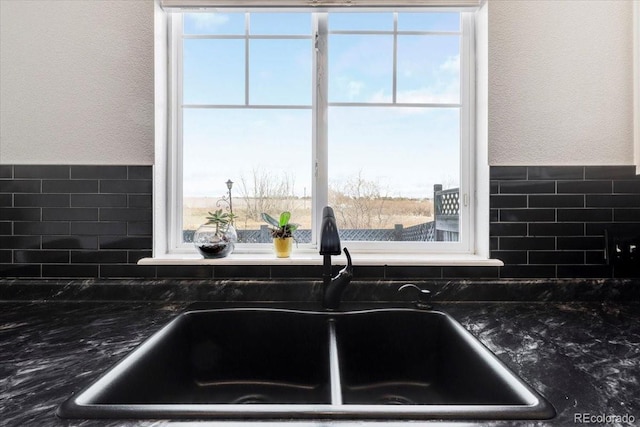 kitchen with dark stone counters, a textured wall, and a sink