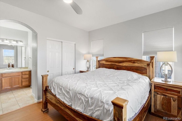 bedroom featuring arched walkways, ceiling fan, light wood-style flooring, a closet, and ensuite bath