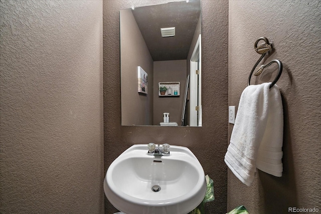 bathroom featuring a textured wall, visible vents, and a sink