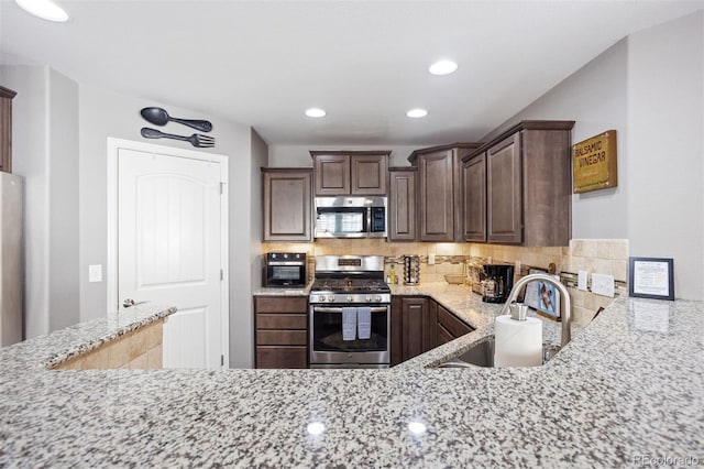 kitchen featuring light stone counters, sink, backsplash, dark brown cabinets, and appliances with stainless steel finishes