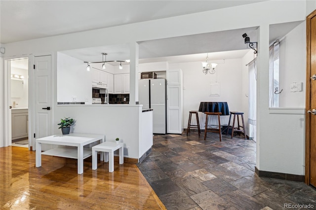 kitchen with kitchen peninsula, white cabinetry, white refrigerator, and an inviting chandelier