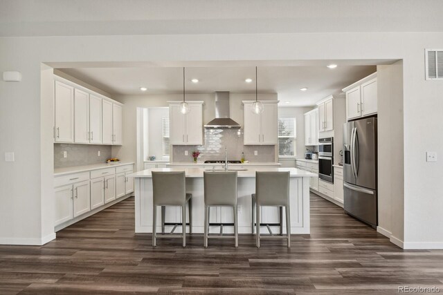11151 W 53rd Dr, Wheat Ridge, CO 80033 - kitchen with wall chimney range hood, appliances with stainless steel finishes, dark wood finished floors, light countertops, and a center island with sink