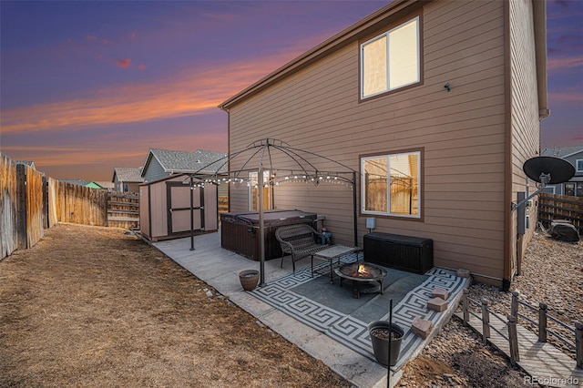 back of house with a hot tub, a fire pit, a fenced backyard, a storage unit, and a patio area