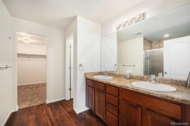 bathroom featuring a shower stall, a walk in closet, a sink, and wood finished floors