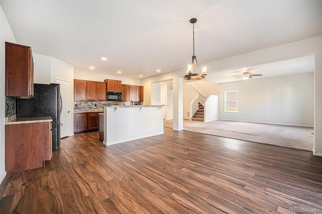 kitchen featuring brown cabinets, dark wood finished floors, decorative backsplash, open floor plan, and black appliances