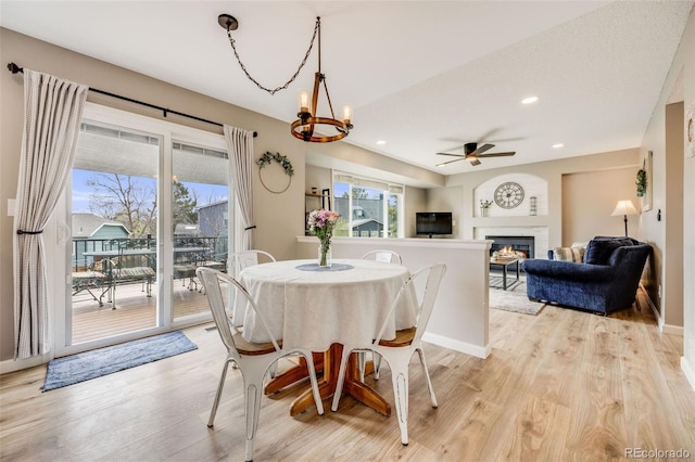 dining space with light wood finished floors, baseboards, a glass covered fireplace, recessed lighting, and ceiling fan with notable chandelier