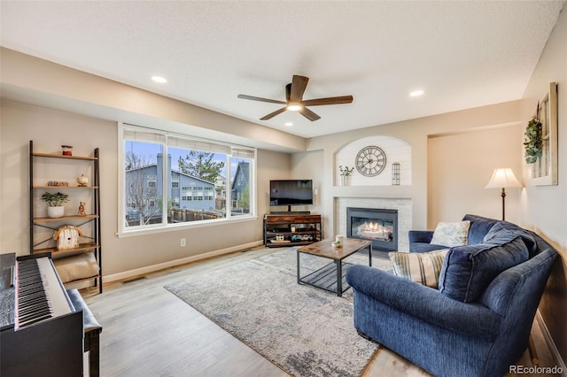 living area featuring recessed lighting, wood finished floors, baseboards, a glass covered fireplace, and ceiling fan