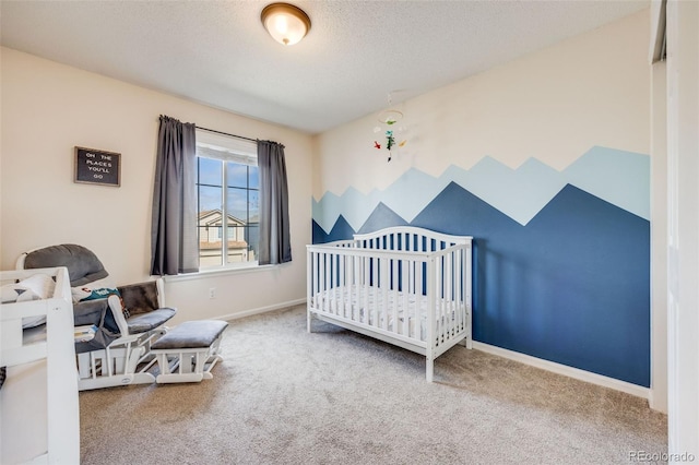 bedroom with a nursery area, carpet floors, a textured ceiling, and baseboards