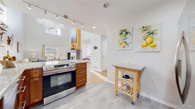 kitchen featuring visible vents, stainless steel appliances, rail lighting, brown cabinetry, and light stone countertops