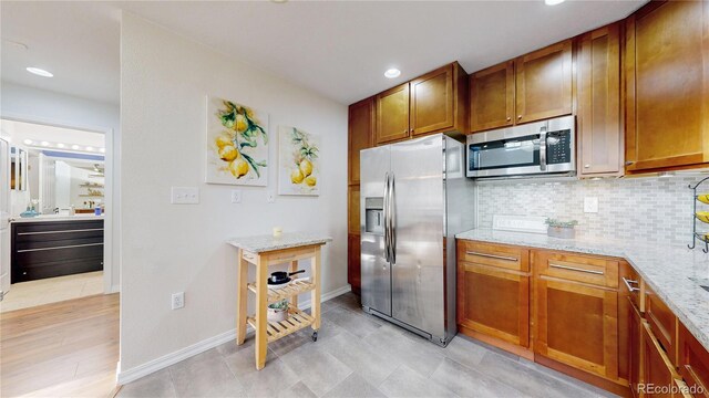 kitchen with light stone countertops, backsplash, brown cabinetry, and appliances with stainless steel finishes