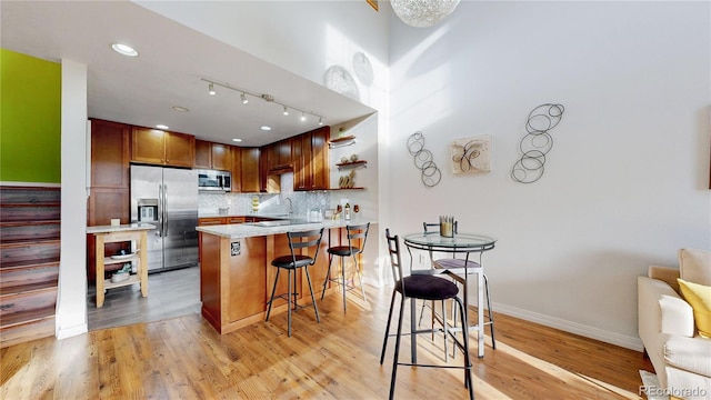 kitchen with a kitchen breakfast bar, tasteful backsplash, stainless steel appliances, a peninsula, and light wood finished floors