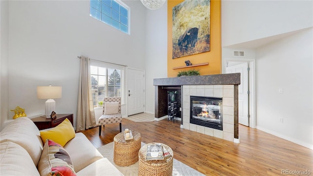 living room with wood finished floors, visible vents, baseboards, a fireplace, and a towering ceiling