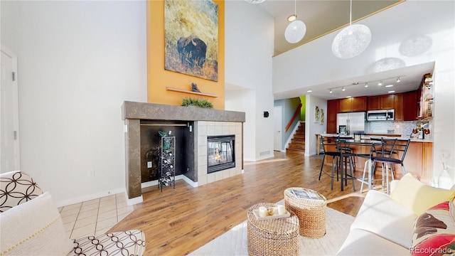 living area with a fireplace, light wood finished floors, baseboards, a towering ceiling, and stairs