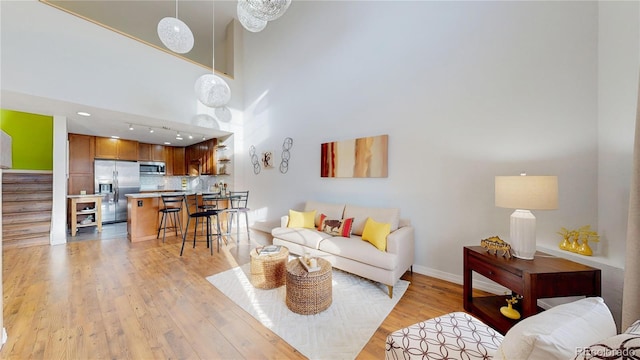 living room with stairway, baseboards, a high ceiling, and light wood finished floors