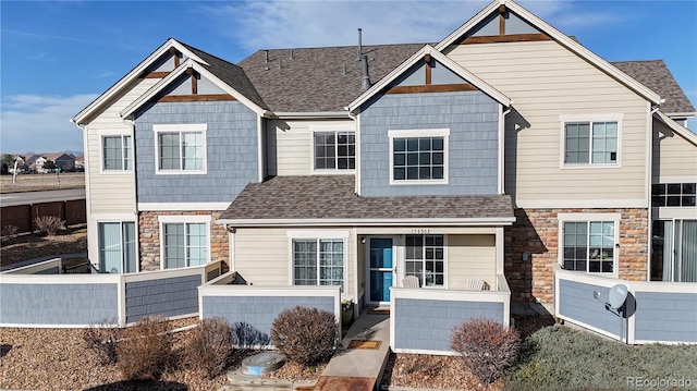 view of front of property with stone siding, a shingled roof, and fence