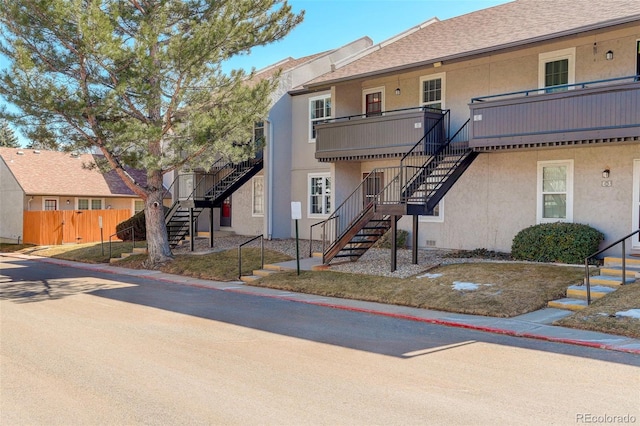 exterior space featuring stairs, fence, roof with shingles, and stucco siding