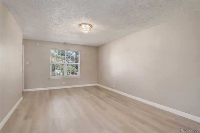 empty room with light wood-style flooring, baseboards, and a textured ceiling