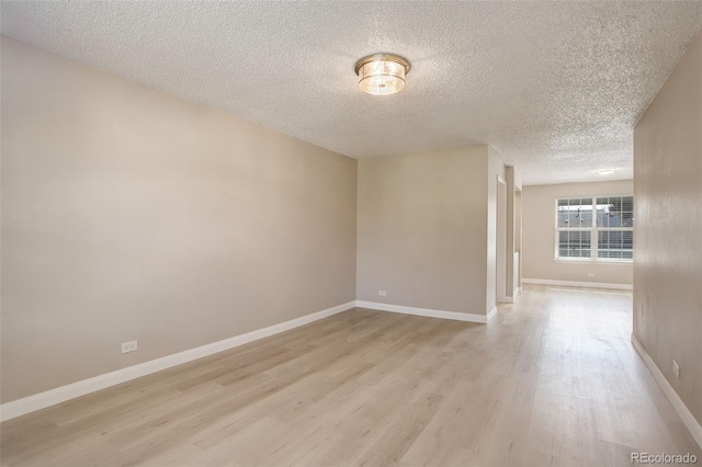 spare room with baseboards, light wood finished floors, and a textured ceiling