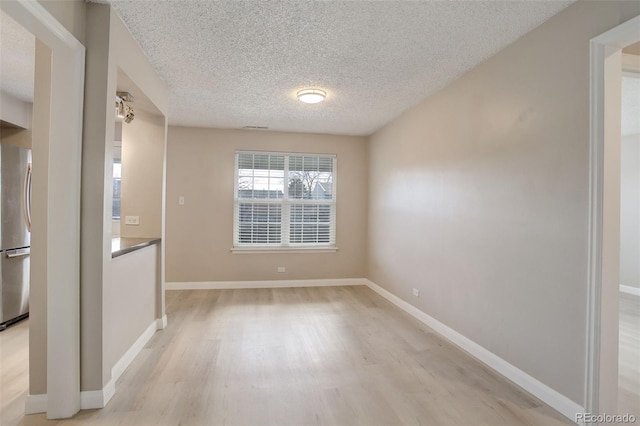 empty room featuring light wood-style flooring, a textured ceiling, and baseboards