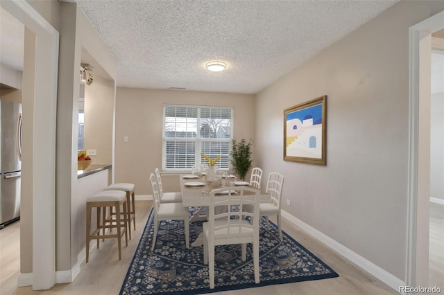 dining area with light wood-style flooring, a textured ceiling, and baseboards