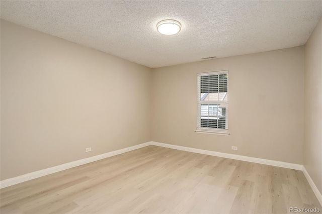 unfurnished room with visible vents, light wood-style flooring, a textured ceiling, and baseboards