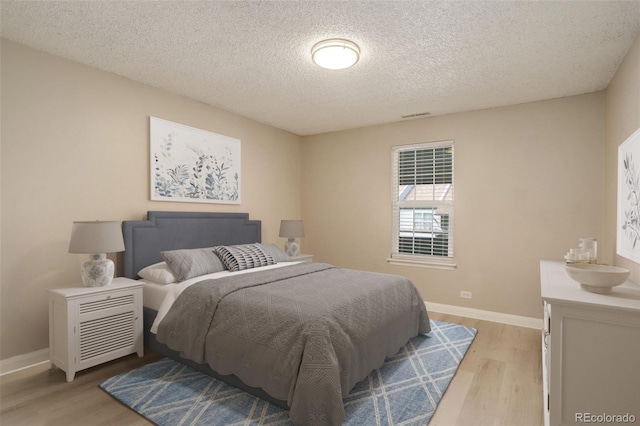 bedroom with light wood finished floors, visible vents, a textured ceiling, and baseboards