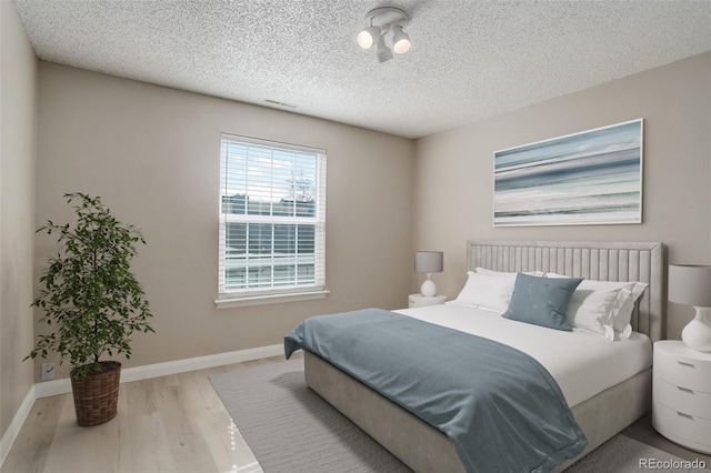 bedroom with visible vents, wood finished floors, baseboards, and a textured ceiling